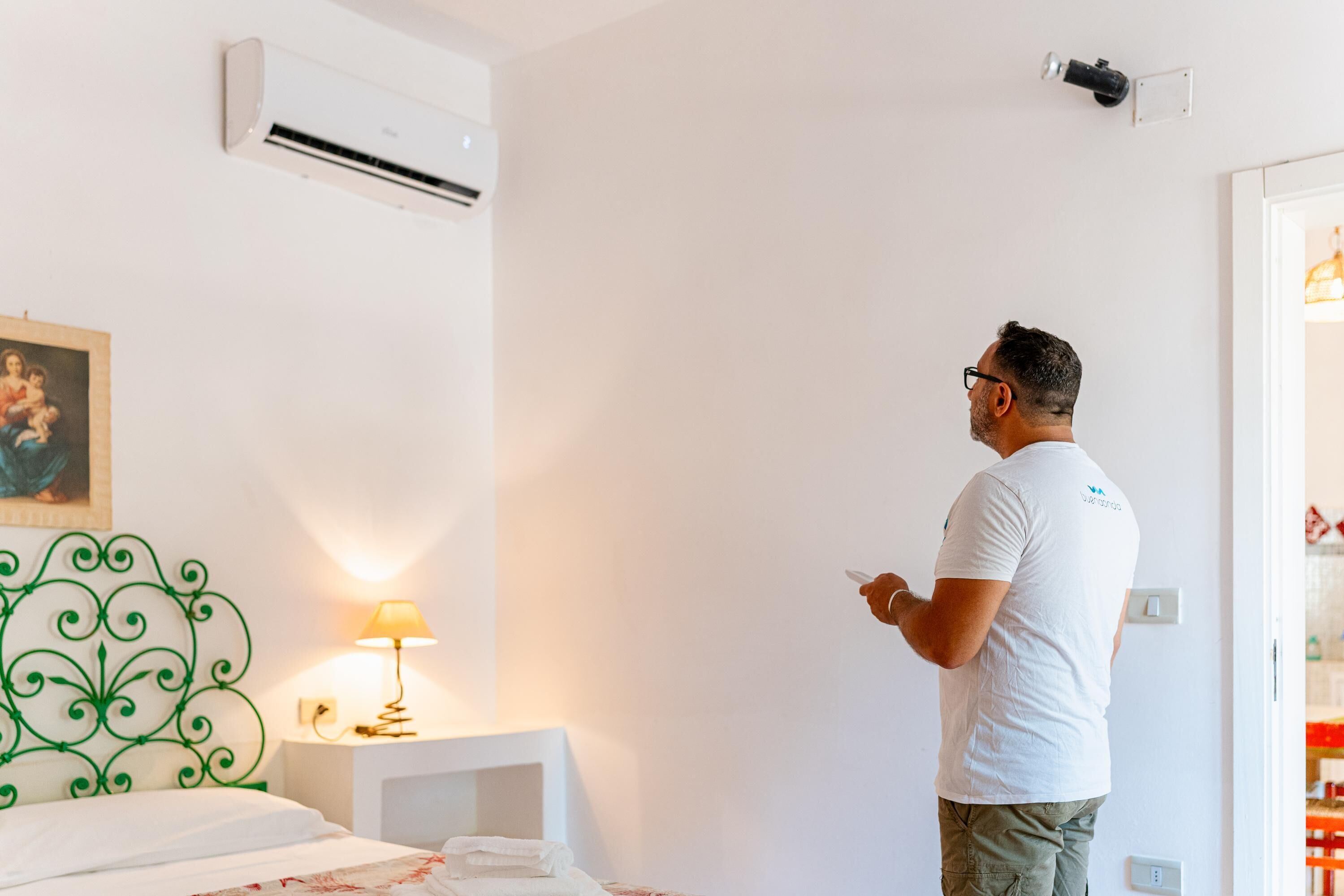 Een hotelkamer met een bed, een wandairconditioner, een bedlamp en een schilderij aan de muur.