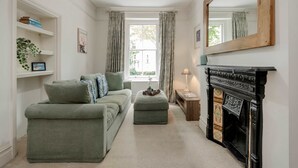 A cozy living room with a green sofa, a fireplace, and a large mirror. - Modern 2 bed Flat - Hammersmith Grove (London)