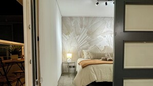 Un dormitori amb un llit, una tauleta de nit, una làmpada i una paret amb un dibuix de fulles.