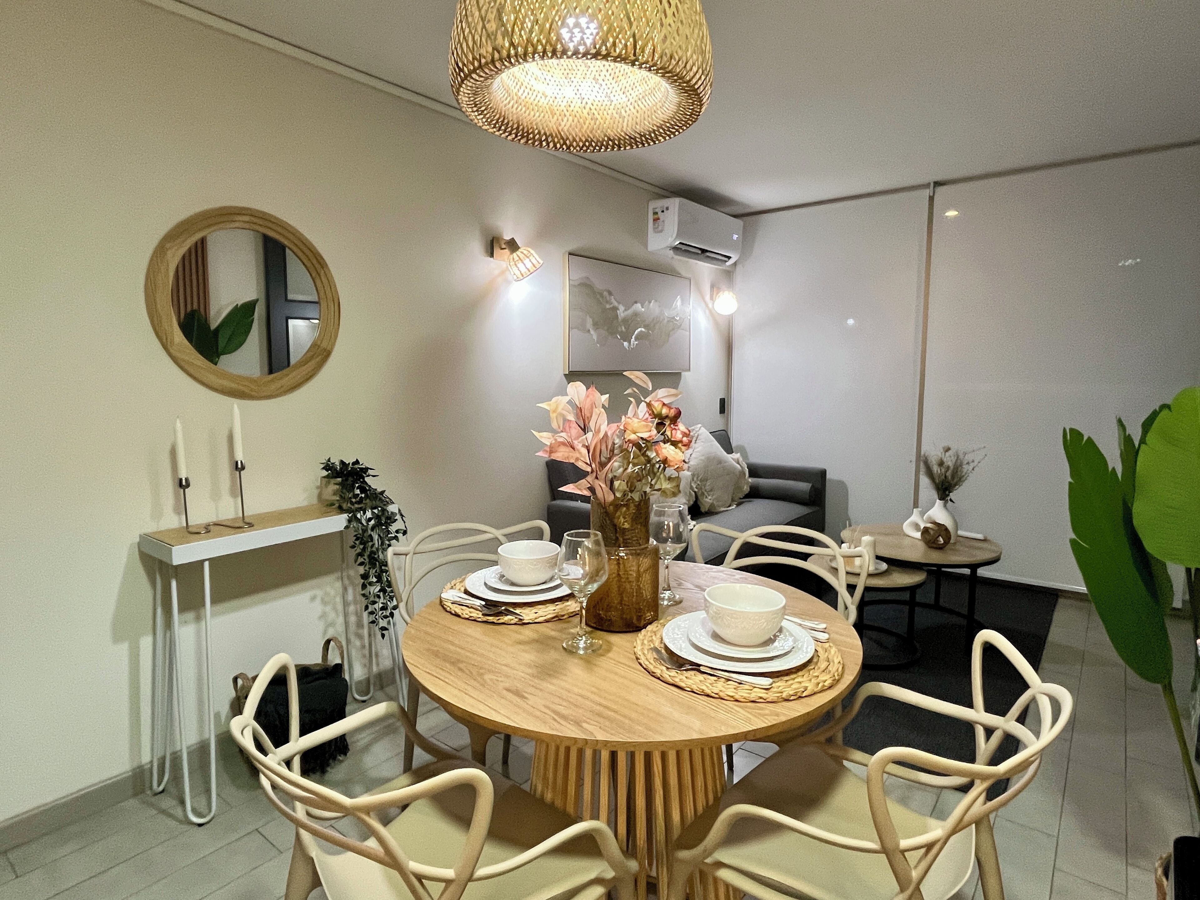 A dining area with a round wooden table, white chairs, a vase with flowers, and a mirror on the wall.