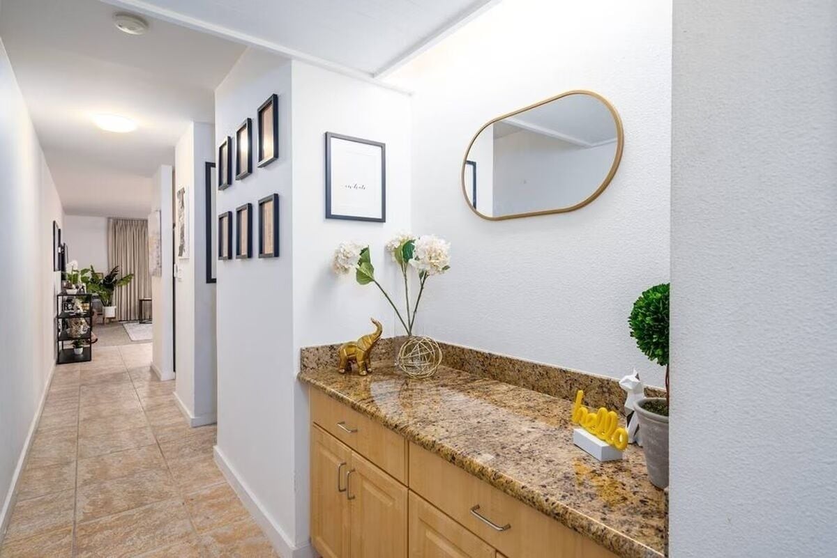 A hallway with a granite countertop, framed pictures, a mirror, and a potted plant.