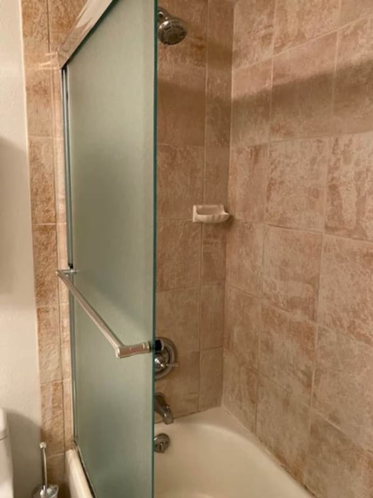 A shower area with a glass door, beige tiles, and a handheld showerhead.