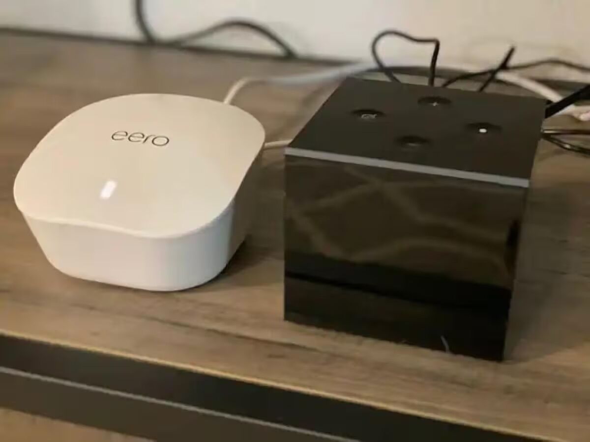 Un dispositivo eero blanco y una caja negra sobre una superficie de madera.