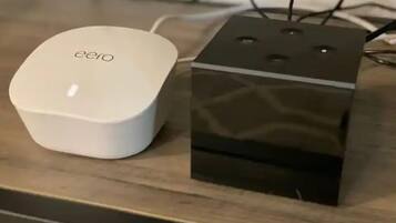 Un dispositivo eero blanco y una caja negra sobre una superficie de madera.