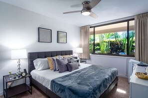 Une chambre moderne avec un grand lit, deux tables de chevet, un ventilateur de plafond et une fenêtre avec des rideaux.