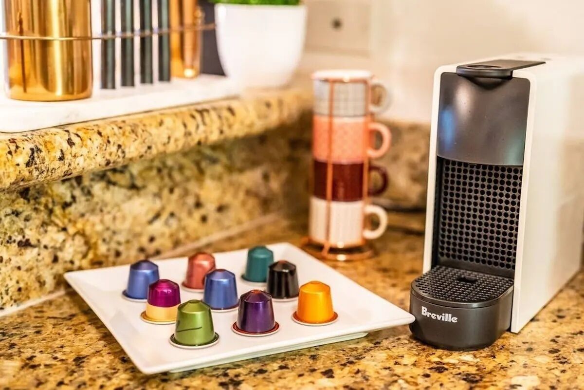 Une machine à café Breville posée sur un plan de travail de cuisine, avec une assiette remplie de capsules de café aux couleurs vives et une tasse.