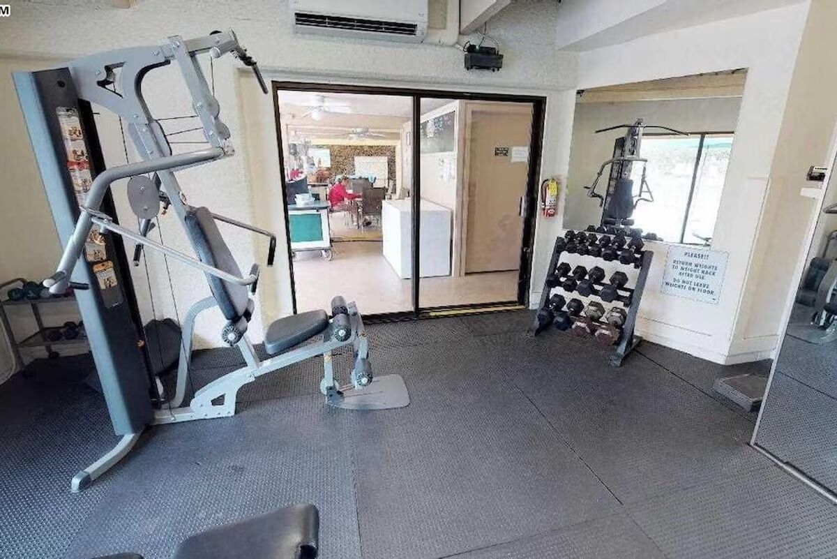 Une salle de sport équipée de matériel d’exercice, avec un porte-haltères et une porte donnant sur une autre pièce.