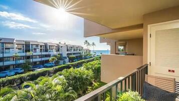 A balcony with a view of a row of modern buildings, a parking area, and lush greenery.