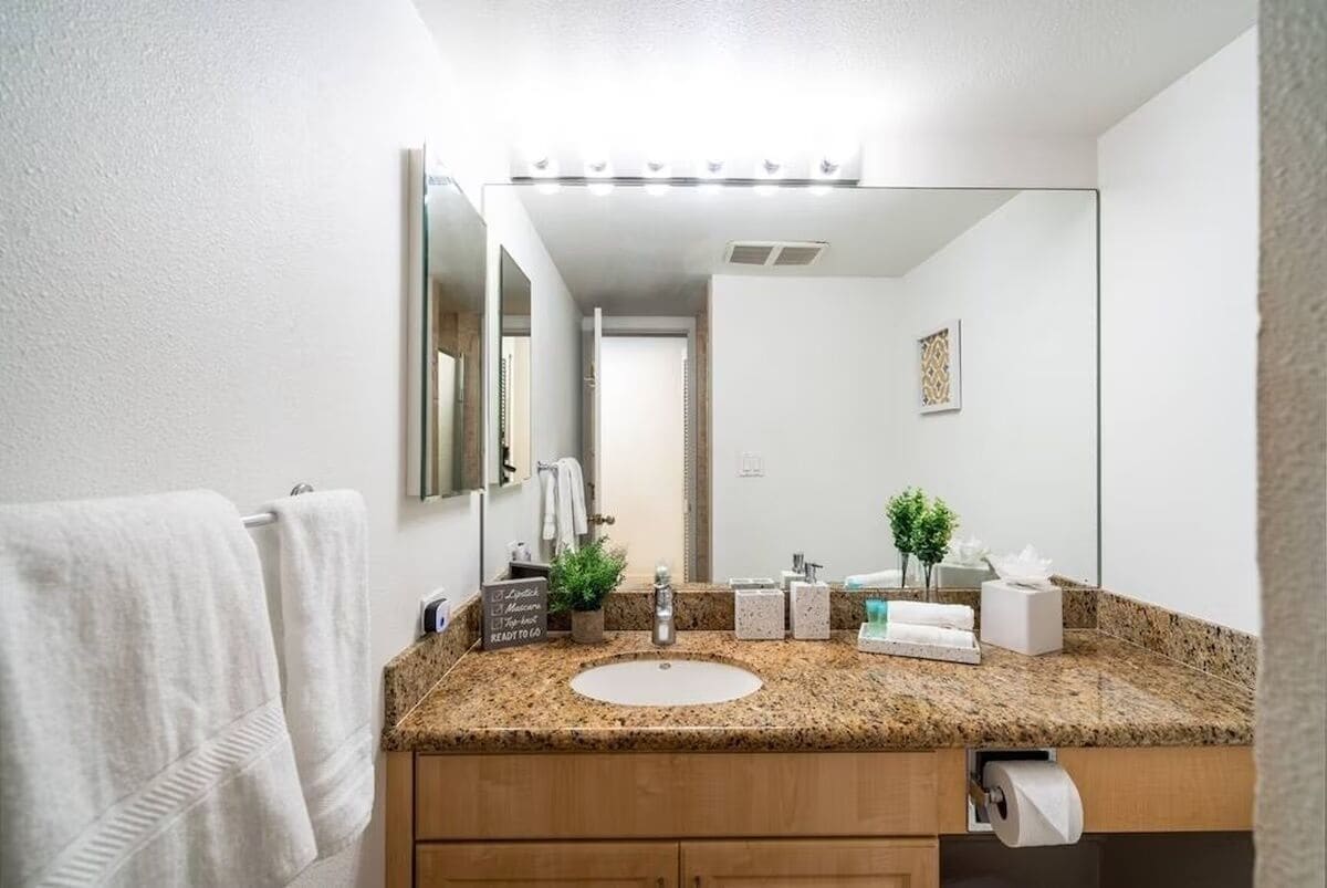A bathroom with a granite countertop, a white sink, a mirror, and a towel rack.
