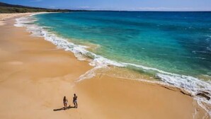 Une plage aux eaux turquoise et limpides, bordée d’un rivage sablonneux.