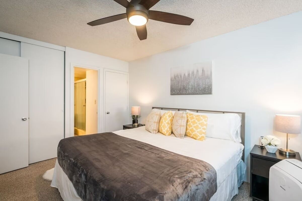 Une chambre à coucher comprenant un lit, un ventilateur de plafond, une table de chevet avec une lampe et une œuvre d’art accrochée au mur.