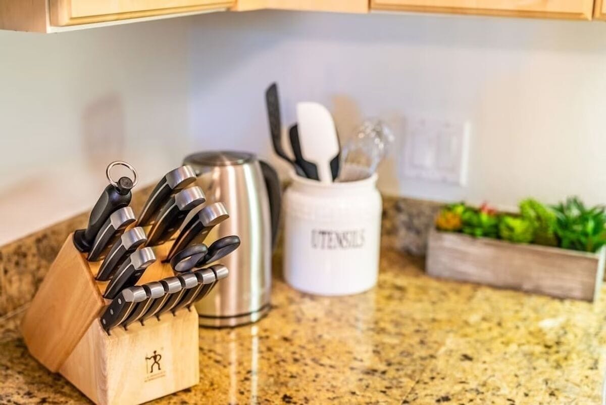 A kitchen counter with a knife block, a stainless steel kettle, and a utensil holder.
