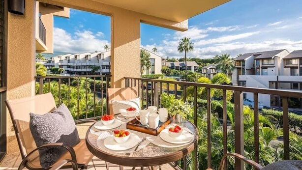 Un balcon avec une table préparée pour le petit-déjeuner, donnant sur un quartier résidentiel bordé de palmiers et comprenant des bâtiments modernes.