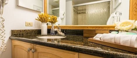 Un baño con encimera de granito, lavabo, espejo, secador de pelo y toallas.