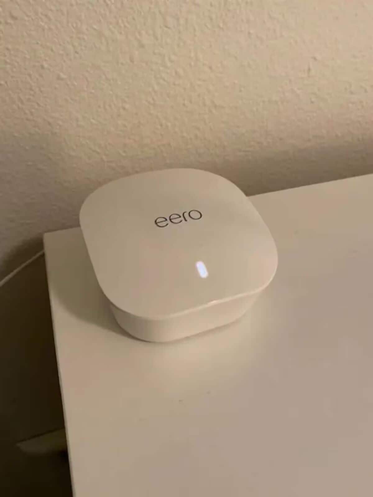Ein weißes, quadratisches Gerät mit dem Schriftzug "eero" auf einer weißen Oberfläche.