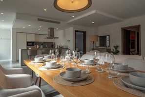 A modern dining area with a wooden table set for a meal, a kitchen in the background, and a living area with a sofa and lamp. - Sky villa penthouse, private pool | MIL by Homega (St. Julian's)