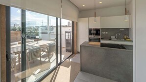 A modern kitchen with a built-in oven, a sink, and a countertop. There is a dining area with a table and chairs visible through a glass door. - Sky villa penthouse, private pool | MIL by Homega (St. Julian's)