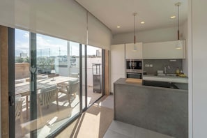 A modern kitchen with a built-in oven, a sink, and a countertop. There is a dining area with a table and chairs visible through a glass door. - Sky villa penthouse, private pool | MIL by Homega (St. Julian's)