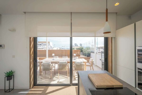 A modern kitchen with a large window, a dining area with wooden furniture, and a view of the cityscape. - Sky villa penthouse, private pool | MIL by Homega (St. Julian's)