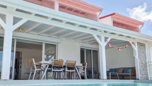 Un área junto a la piscina con un porche cubierto, mobiliario exterior y vistas a la piscina.