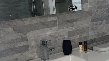 A modern bathroom with a large white sink, a mirror, and a shower area.