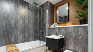 Un baño moderno con ducha envuelta en vidrio, una bañera blanca, un tocador negro y un inodoro blanco.