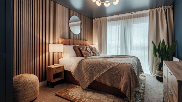 Un dormitorio con cama, mesita de noche, lámpara y un espejo grande.