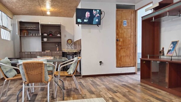 A living room with a dining area, a television mounted on the wall, and a wooden door. - Samaya Department sharing (Cusco)