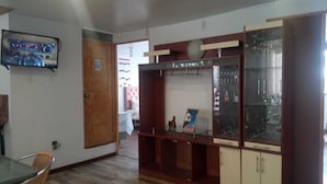 A room with a wooden cabinet, a television mounted on the wall, and a dining area with a table and chairs. - Samaya Department sharing (Cusco)