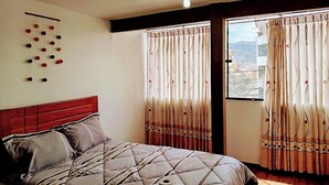 A bedroom with a bed, curtains, a wall-mounted object, and a window with a view. - Samaya Department sharing (Cusco)