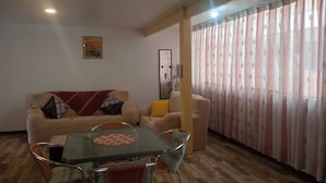 A living room with a sofa, a coffee table, and a dining table with chairs. There is a window with curtains and a painting on the wall. - Samaya Department sharing (Cusco)