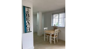 Un coin repas avec une table et des chaises en bois, une fenêtre avec des stores et un panneau fixé au mur.