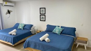 Une chambre avec deux lits, chacun agrémenté de draps bleus et d’oreillers décoratifs. Une petite table de chevet avec une lampe se trouve à côté de chaque lit.