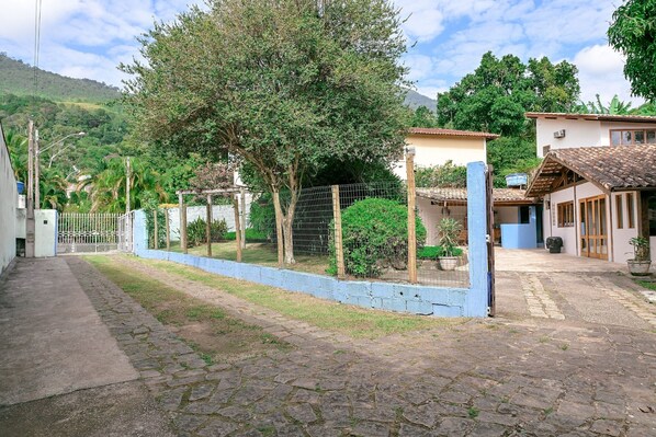 A paved courtyard with a stone pathway, a fenced area with trees, and buildings with tiled roofs.