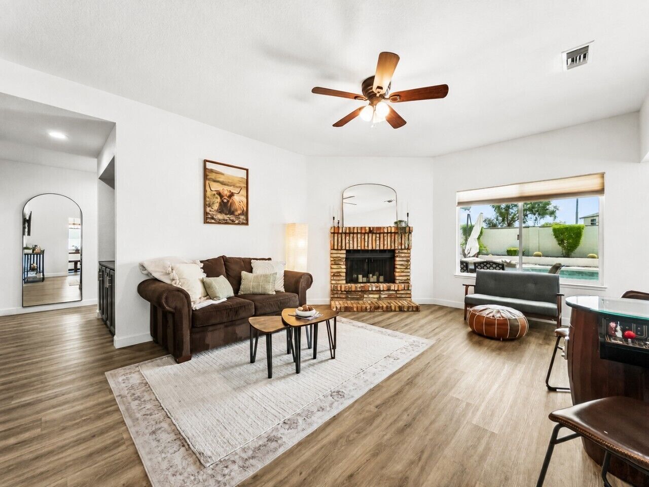 A living room with a fireplace, a ceiling fan, a large window, and a dining area.
