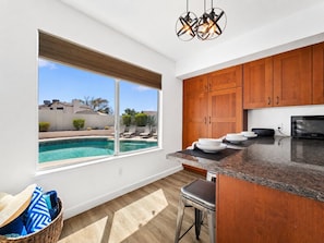 A kitchen with wooden cabinets, a granite countertop, a built-in microwave, and a view of a swimming pool.
