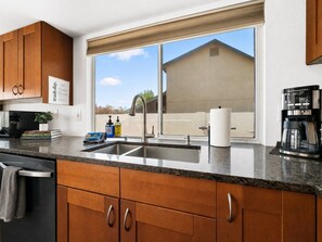 Eine Küche mit Holzausstattung, einem Edelstahlspülbecken, einer Kaffeemaschine und einem Fenster mit Blick auf ein Haus.