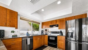 A modern kitchen with wooden cabinets, stainless steel appliances, and a black countertop. - Dive In Desert - 3Bd - Pool Oasis (Chandler)