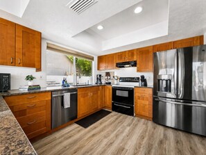 Cozinha moderna com armários de madeira, eletrodomésticos de aço inoxidável e bancada preta.