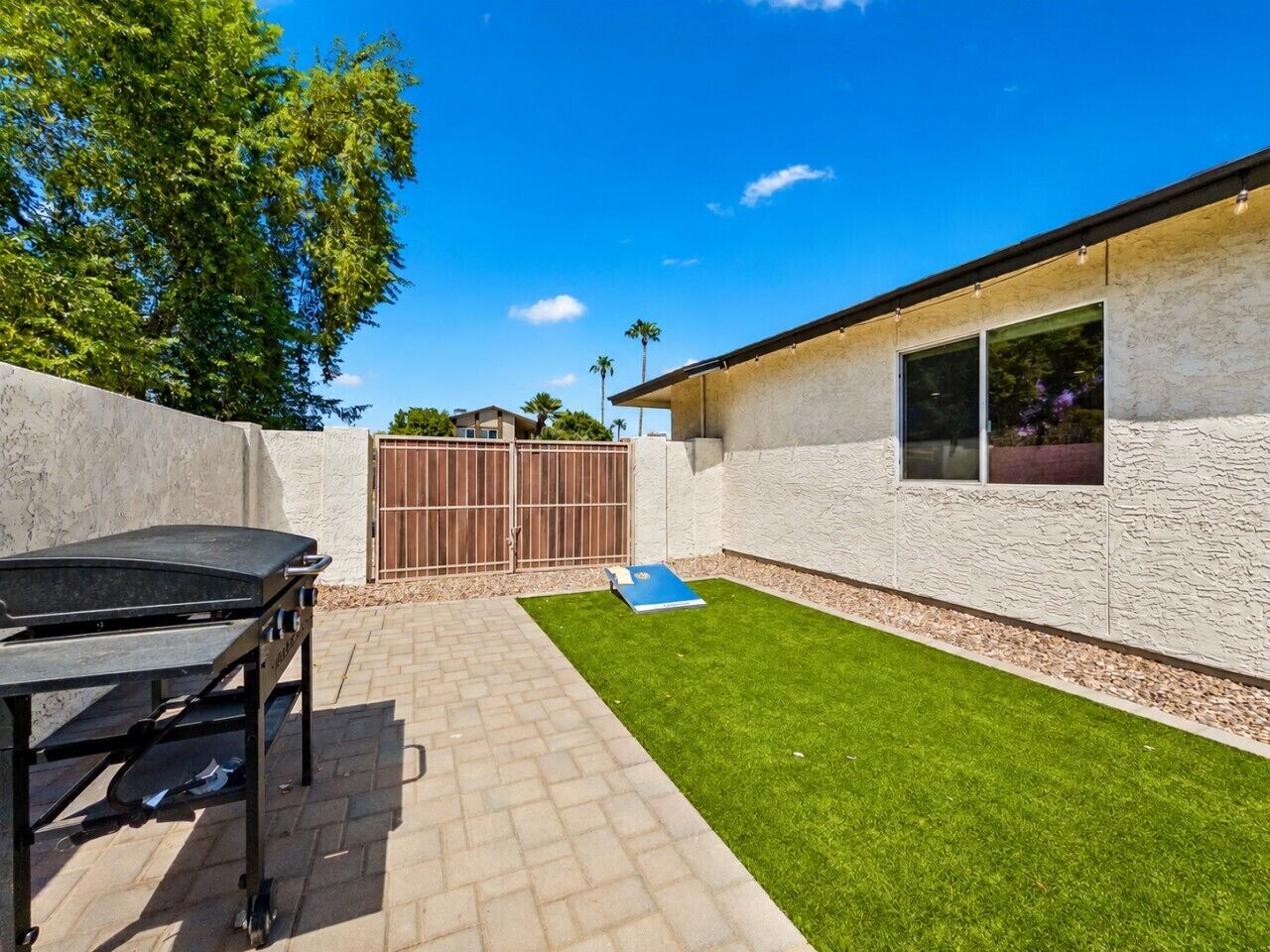 A backyard with a barbecue grill, a paved patio, a grassy area, and a building with a window.