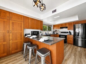 A modern kitchen with wooden cabinets, stainless steel appliances, and a central island with bar stools. - Private Pool | 3BR, 2 Living Rooms | Chandler (Chandler)