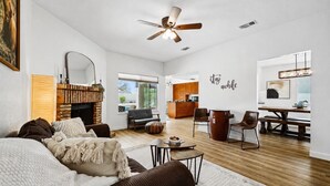 A spacious living room with a fireplace, a dining area, and a kitchen in the background. - Dive In Desert - 3Bd - Pool Oasis (Chandler)