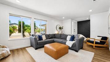 A modern living room with a sectional sofa, a leather ottoman, and a view of the outdoors.