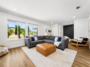 A modern living room with a sectional sofa, a leather ottoman, and a view of the outdoors.