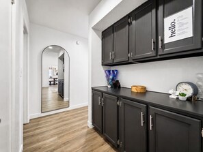 A hallway with a wooden floor, a black cabinet with a 'hello' sign, and a mirror reflecting a dining area.
