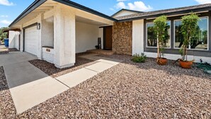 A modern house with a covered porch, stone exterior, and potted plants. - Dive In Desert - 3Bd - Pool Oasis (Chandler)