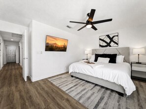 A bedroom with a bed, bedside tables, a ceiling fan, a wall-mounted artwork, and a door leading to another room. - Private Pool | 3BR, 2 Living Rooms | Chandler (Chandler)