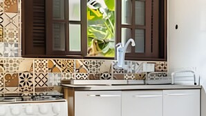 A kitchen with a white stove, a sink with a faucet, and a window with a view of greenery. - Chalé da Libélula 3: Refuge close to the beach (Ilhabela)