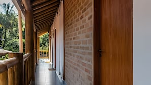 A corridor with wooden railings and a brick wall, leading to a balcony with a view of greenery.