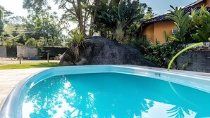 A swimming pool with clear blue water, surrounded by lush greenery and a large rock.